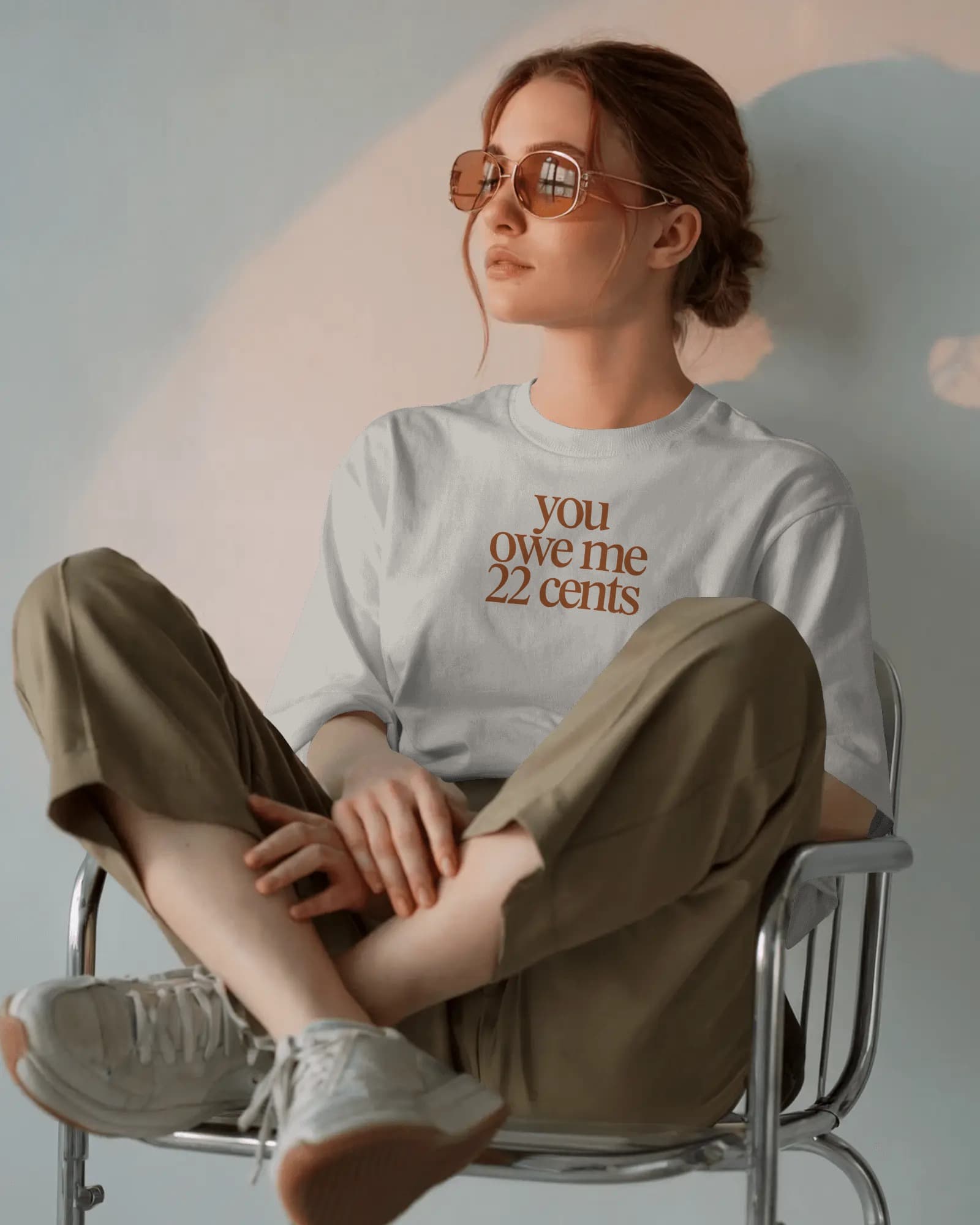 Woman in vintage sunglasses wearing You Owe Me 22 Cents tee, seated in natural light — Salt + Violet